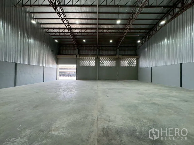 Warehouse for rent in Bang Phli, Samut Prakan - Wide warehouse floor facing multiple metal shutters and a loading opening