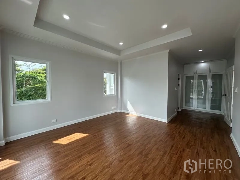 Detached House for sale in Lam Luk Ka, Pathum Thani - Sunlit bedroom with wood flooring, recessed lights and built-in wardrobe area.