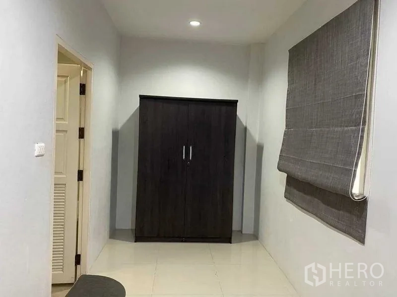 Home Office for rent in Khlong Toei, Bangkok - Compact room with dark wardrobe and grey roman blind near the doorway.