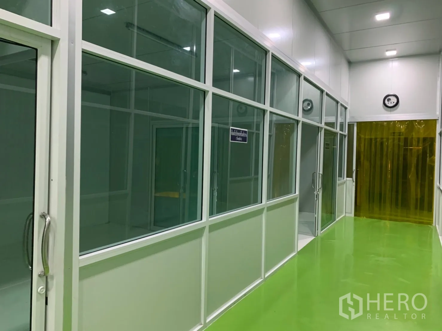 Factory for rent in Khlong Luang, Pathum Thani - Corridor lined with glass-fronted rooms leading to a yellow-curtained doorway.