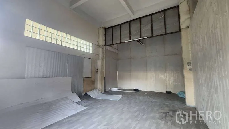 Factory for rent in Chom Thong, Bangkok - Double-height loading room with glass-block windows and a tall sliding gate.