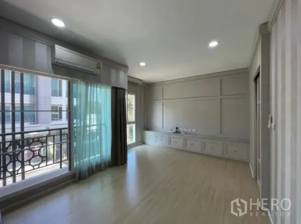 Townhouse for sale - Spacious living room with balcony access, air-conditioner, wood floors, and built-in low cabinets.