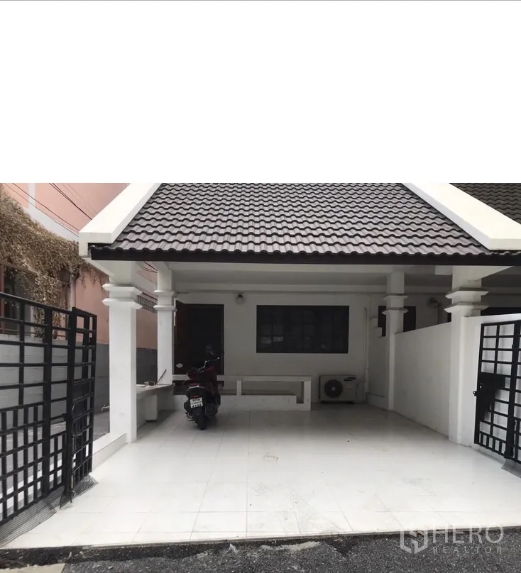 Townhouse for rent in Watthana, Bangkok - Close view of covered carport with white columns, black metal gate and tiled floor.