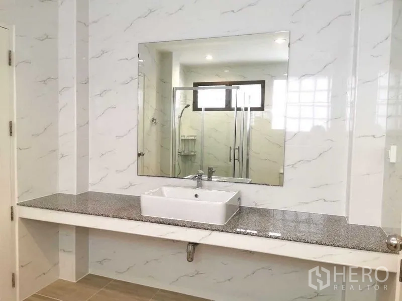Detached House for rent in Bang Rak, Bangkok - Large bathroom with marble-look walls, wide mirror, vanity sink, and glass shower enclosure.