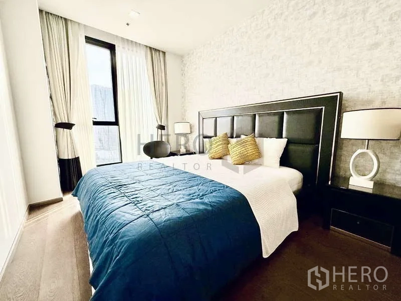 Condominium for rent - Corner bedroom with large window, blue comforter and modern bedside lamps.
