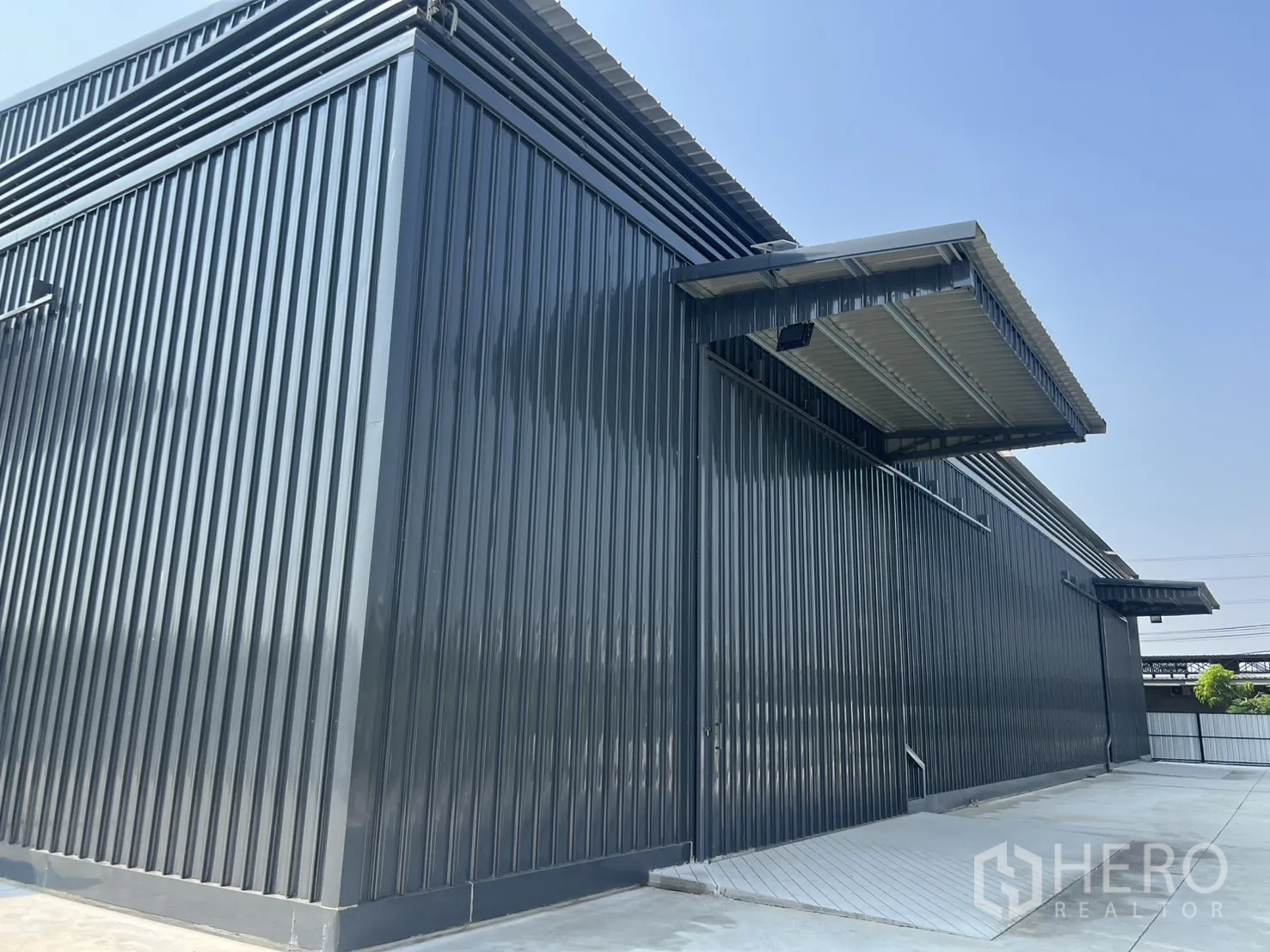 Warehouse for rent in Lat Krabang, Bangkok - Corner view of ribbed steel warehouse walls with a loading ramp and sheltered dock.