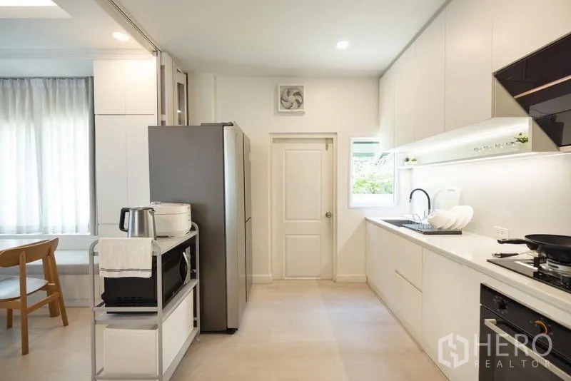 Detached House for sale in Prawet, Bangkok - Bright modern kitchen with white cabinetry, double sink, large fridge and gas hob.