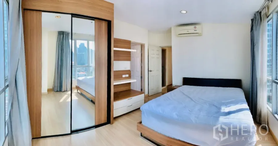 Condominium for rent in Bang Rak, Bangkok - Corner master bedroom with large windows, mirrored wardrobe, and built-in storage.