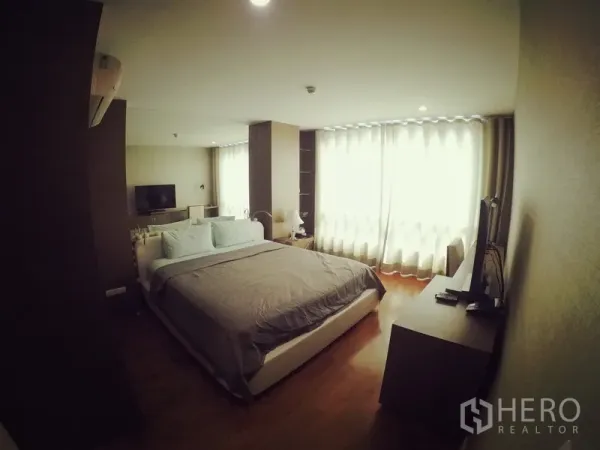 Condominium for rent or sale in Khlong Toei, Bangkok - Primary bedroom with king bed, large windows with sheer curtains, TV and dresser.