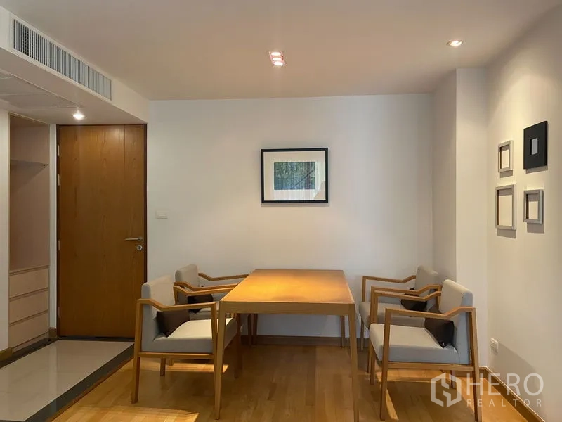 Condominium for rent or sale in Khlong Toei, Bangkok - Minimalist dining area with wooden table and four upholstered chairs under soft lighting.