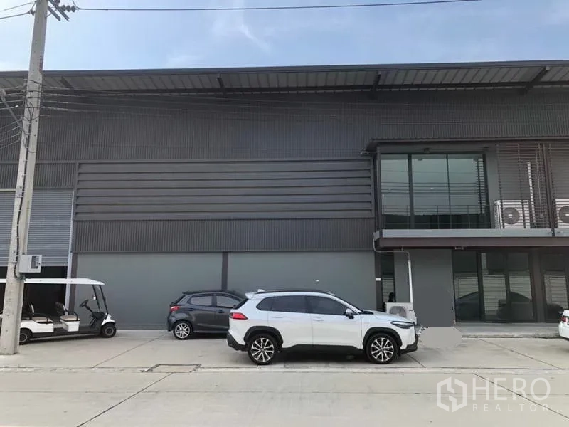 Warehouse for rent in Bang Phli, Samut Prakan - Facade showing glass-front office on the upper floor with parked cars along the warehouse.