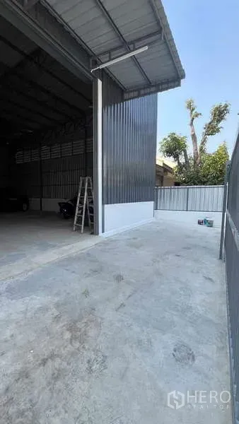 Warehouse for rent in Bang Khen, Bangkok - Concrete driveway and tall shutter entrance of a metal-clad warehouse with covered loading bay.