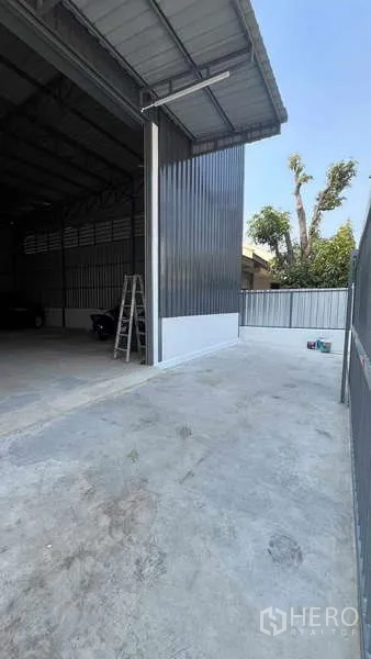 Warehouse for rent in Bang Khen, Bangkok - Concrete driveway and tall shutter entrance of a metal-clad warehouse with covered loading bay.
