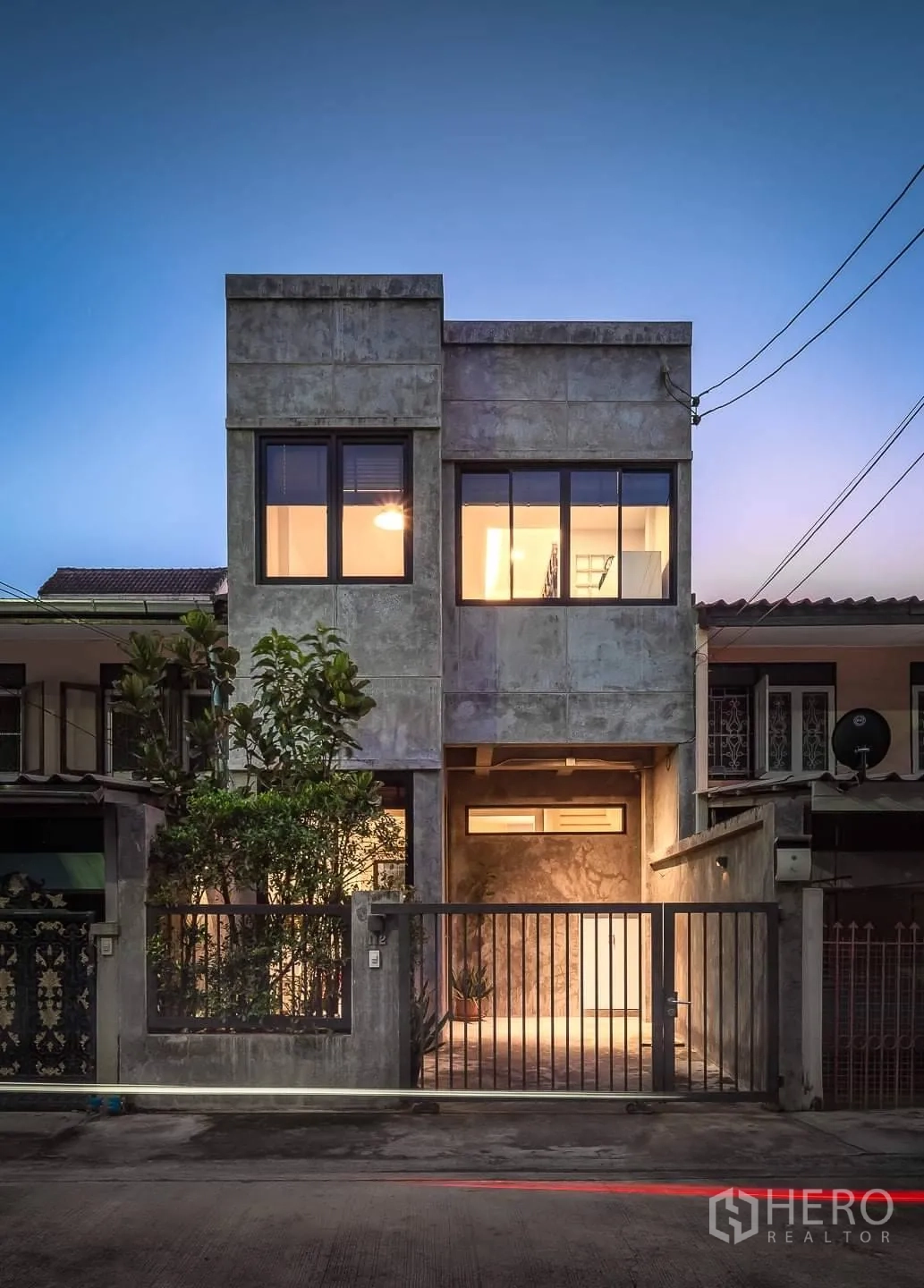 联排别墅 出租在Huai Khwang, Bangkok - 黄昏时的现代水泥风联排别墅外观，大窗与带门车位。