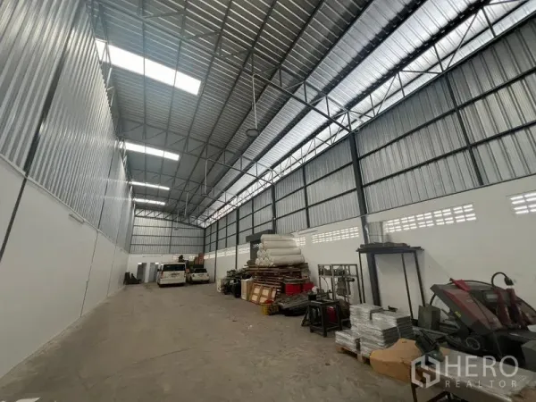Warehouse for rent in Khlong Sam Wa, Bangkok - Spacious warehouse interior with clear-span steel truss roof, skylight panels, concrete floor and organized storage areas.