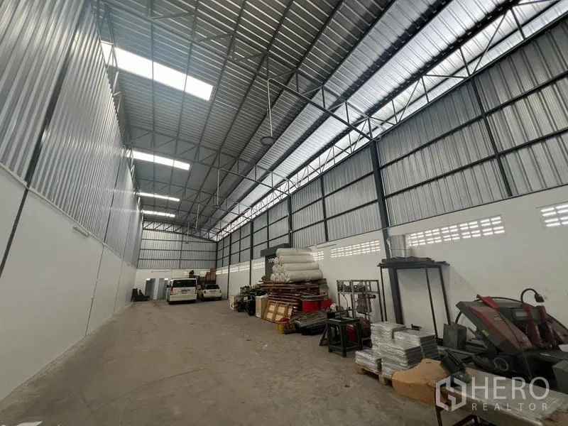 Warehouse for rent in Khlong Sam Wa, Bangkok - Spacious warehouse interior with clear-span steel truss roof, skylight panels, concrete floor and organized storage areas.