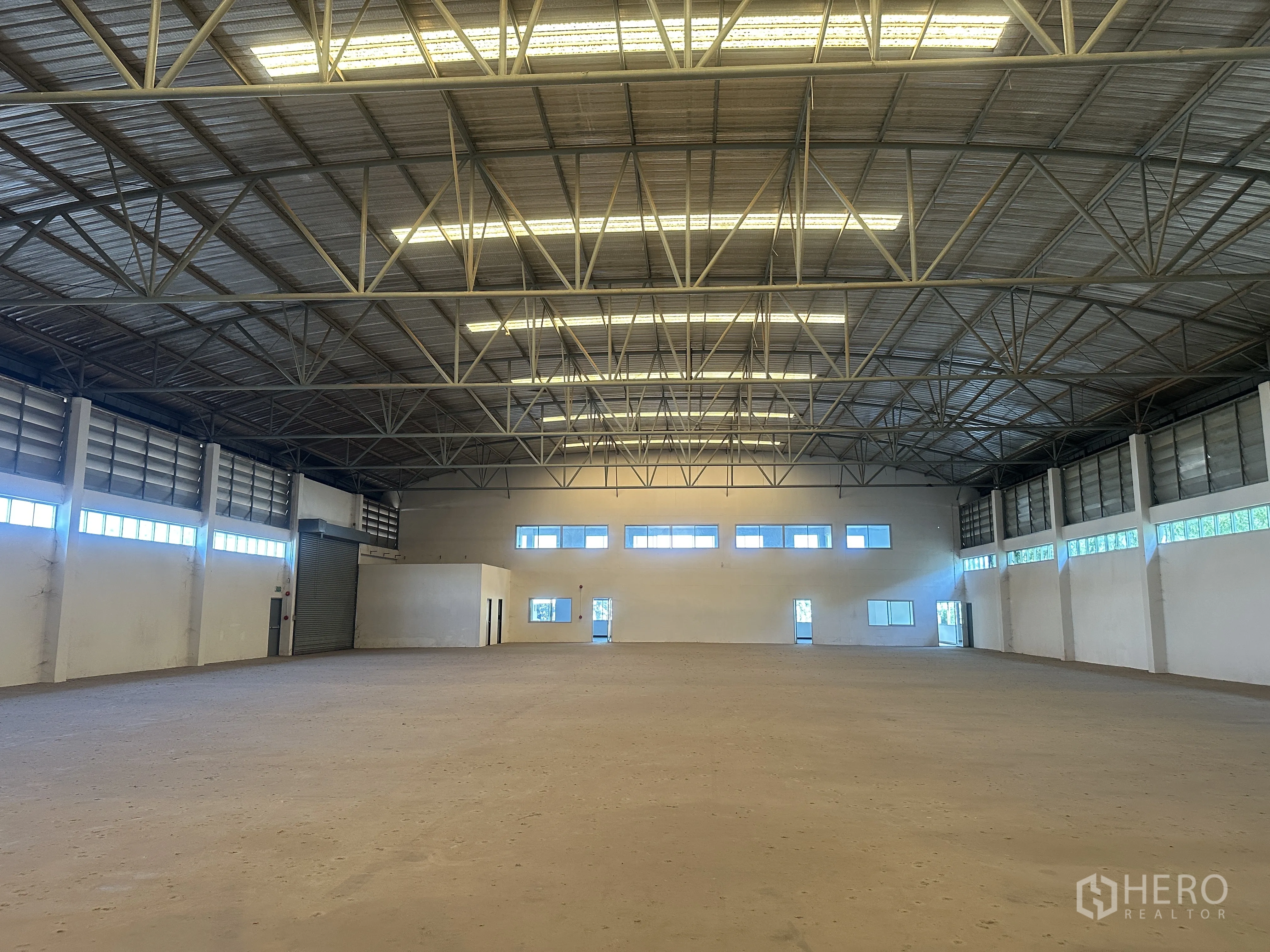 Factory for rent in Bang Pa-in, Phra Nakhon Si Ayutthaya - Spacious production hall with high steel truss roof, concrete floor, side windows, and roller shutter doors.