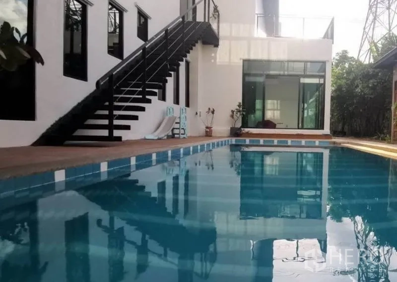 Detached House for sale in Pak Kret, Nonthaburi - Large pool beside white modern facade with exterior staircase and a glass-walled room.