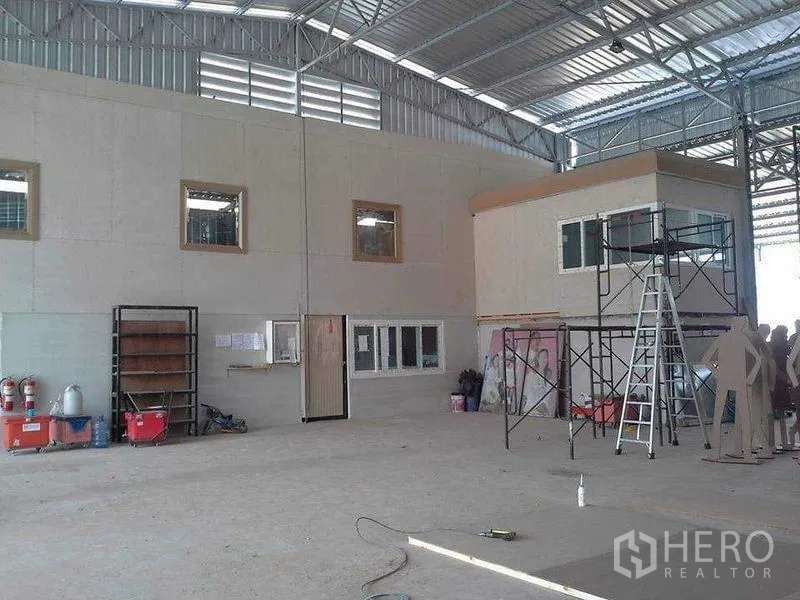 Warehouse for sale in Lam Luk Ka, Pathum Thani - Wide clear-span production hall with enclosed mezzanine-style office and open concrete floor.