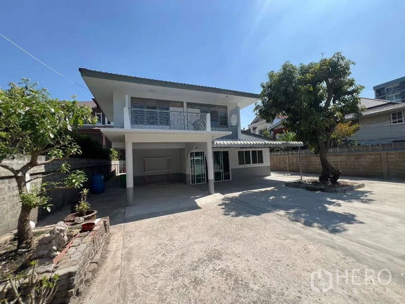 Detached House for rent in Bang Na, Bangkok - Front yard with wide concrete driveway, mature tree and two-storey facade.