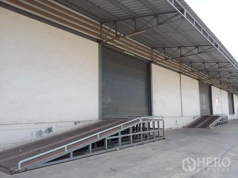 Warehouse for rent in Mueang Samut Sakhon, Samut Sakhon - Covered warehouse loading bay with metal ramps and roller shutter doors for truck access.