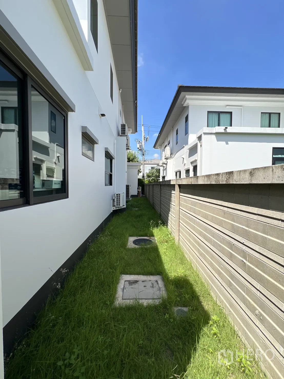 Detached House for rent or sale in Mueang Pathum Thani, Pathum Thani - Side yard with grass strip, boundary wall and outdoor air-conditioning units.