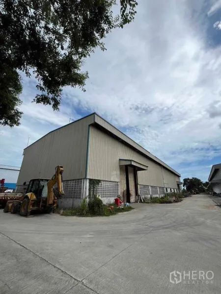 Factory for sale in Nikhom Phatthana, Rayong - Metal-clad factory with wide concrete driveway and backhoe parked outside in Nikhom Phatthana, Rayong.
