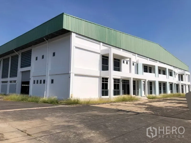 Factory for rent or sale in Phra Nakhon Si Ayutthaya - Modern white factory exterior with green metal roof and wide driveway under a clear sky in Bang Pa-in.