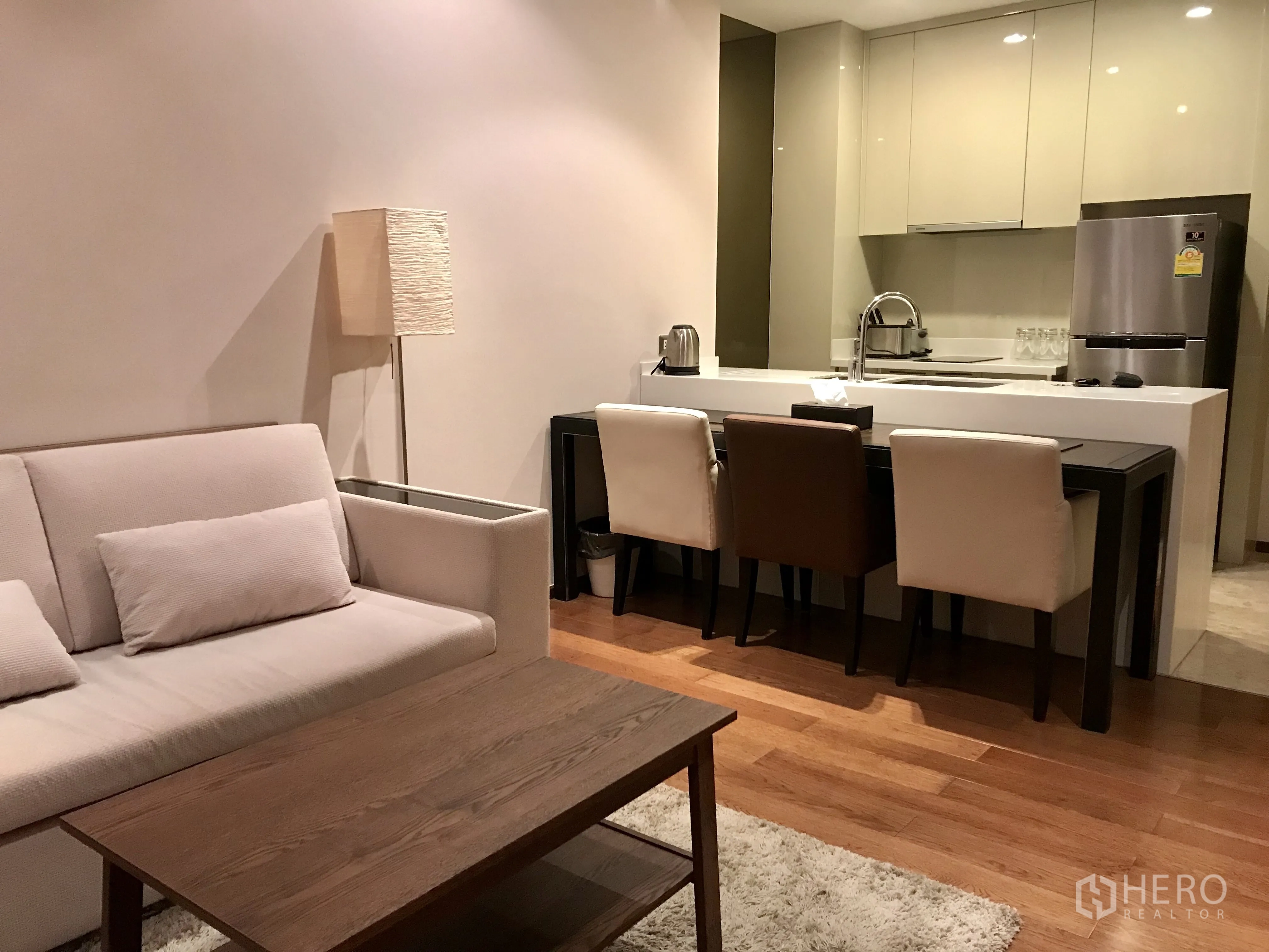 Condominium for rent or sale in Khlong Toei, Bangkok - Open-plan lounge and kitchen with sofa, dining set, island sink and warm hardwood floors.