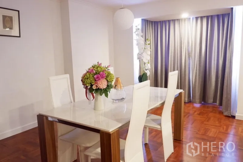 Condominium for rent in Khlong Toei, Bangkok - Dining area with white chairs, marble-top table, flowers and long drapes.