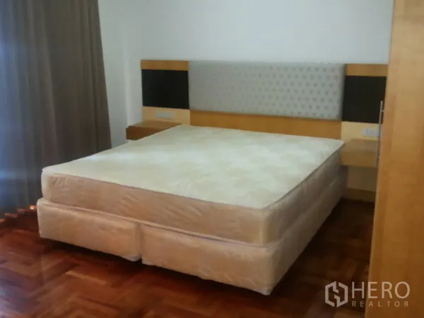 Apartment for rent in Khlong Toei, Bangkok - Second bedroom with upholstered headboard, bedside shelves, and parquet flooring.
