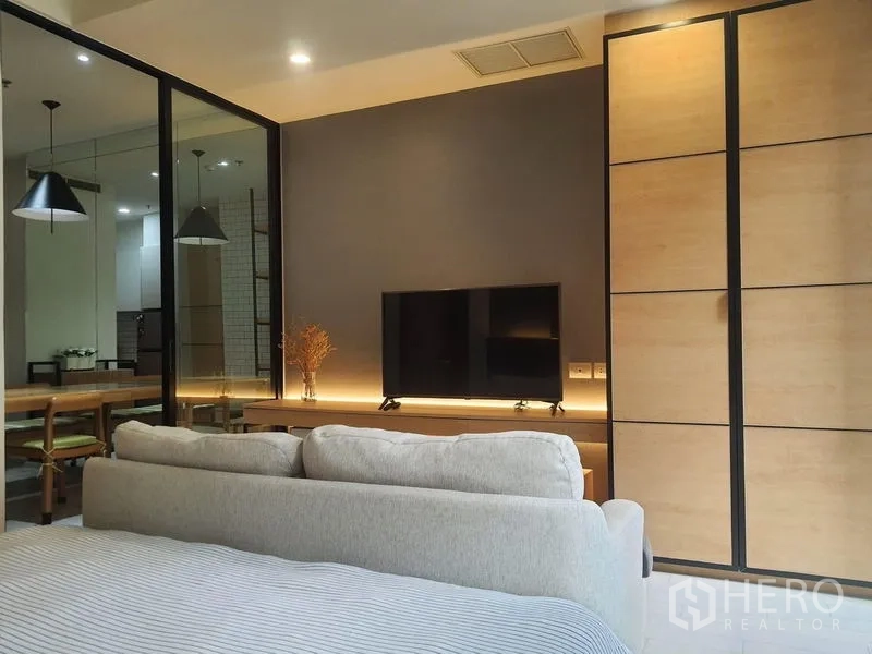 Condominium for rent in Pathum Wan, Bangkok - TV feature wall with warm accent lighting viewed from the bed and modern built-in cabinetry.