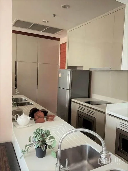 Condominium for rent in Khlong Toei, Bangkok - Compact galley kitchen with double sink, built‑in hob, and ample storage cabinets.