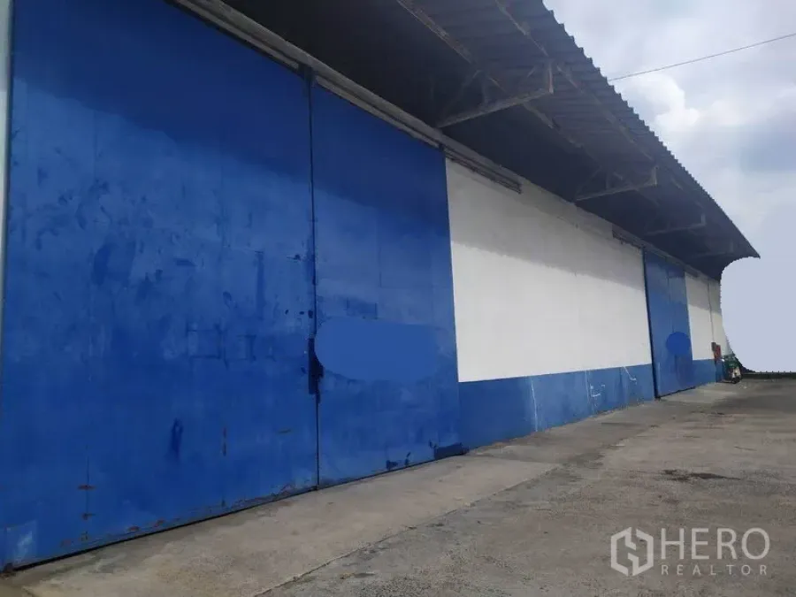 Warehouse for rent in Mueang Samut Prakan, Samut Prakan - Warehouse exterior with large blue sliding metal doors, covered loading area and wide driveway for trucks.
