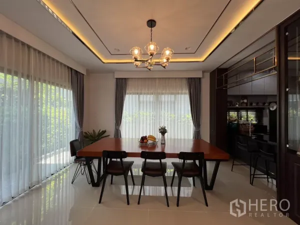 Detached House for rent or sale in Bang Kapi, Bangkok - Dining area with wooden table, six chairs, chandelier and floor-to-ceiling sheer curtains.