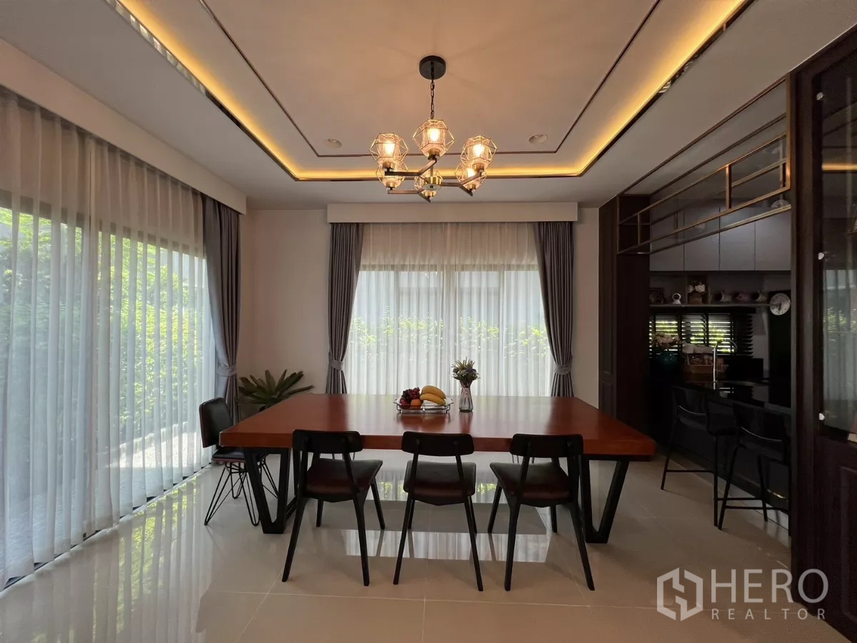 Detached House for rent or sale in Bang Kapi, Bangkok - Dining area with wooden table, six chairs, chandelier and floor-to-ceiling sheer curtains.