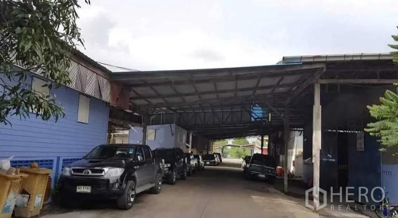 货栈 出租在Sai Noi, Nonthaburi - 赛诺伊仓库区入口，金属雨棚覆盖的车道与停放车辆