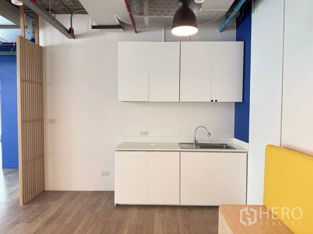 Office Space for rent in Din Daeng, Bangkok - Compact kitchenette with white cabinets, sink, and wood-look flooring beside a slatted divider.