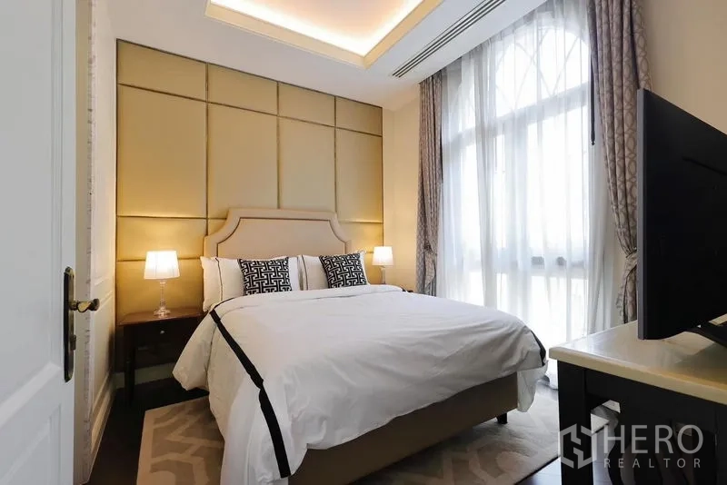 Detached House for rent or sale in Watthana, Bangkok - Cozy bedroom with padded headboard, large arched window and bedside lamps.