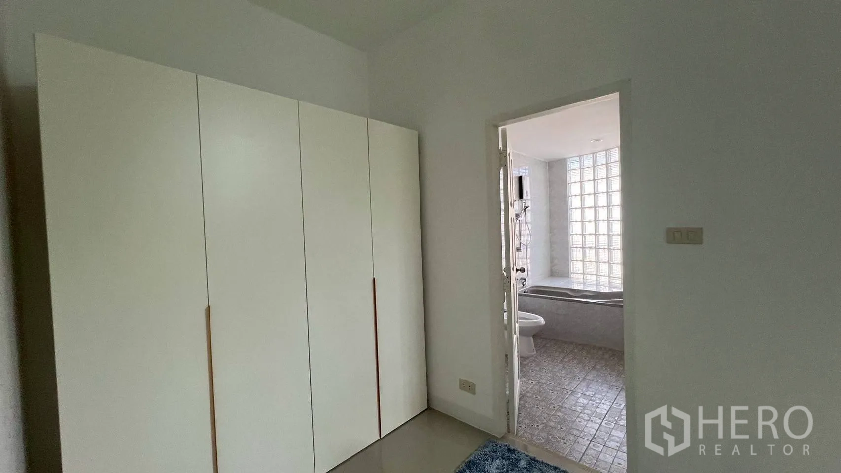 Home Office for rent in Wang Thonglang, Bangkok - Compact room with tall white wardrobe leading to a tiled bathroom with bathtub and glass-block wall.