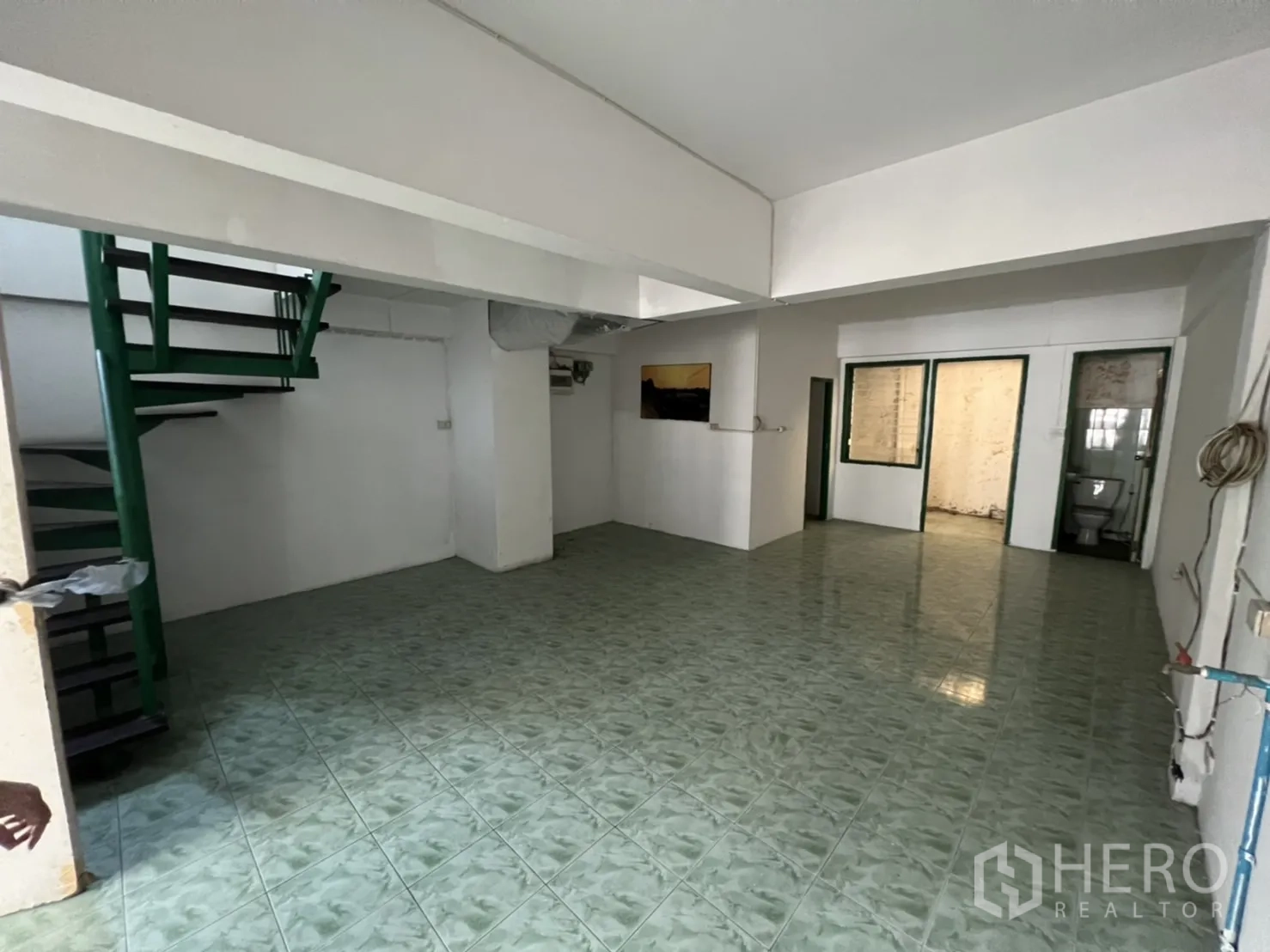 联排别墅 出售在Watthana, Bangkok - 一层开放空间，绿色地砖、旋转楼梯与公共卫生间。