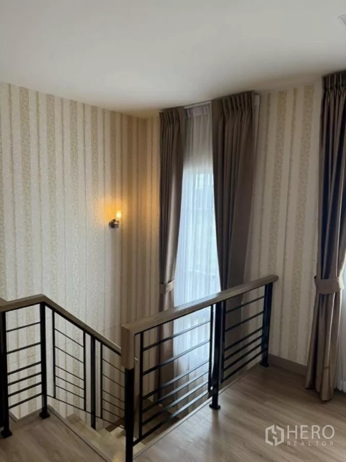 Detached House for rent in Thanyaburi, Pathum Thani - Upstairs landing with striped wallpaper, railing and large curtained windows.