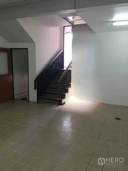 Townhouse for rent in Phra Khanong, Bangkok - Ground floor with tiled flooring, a staircase with wrought‑iron railing and light from a vertical window.