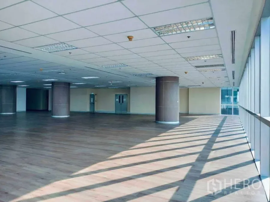Office Space for rent in Sathon, Bangkok - Sunlit open‑plan office floor with wood flooring, round columns and floor‑to‑ceiling windows.