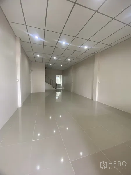联排别墅 出租在Suan Luang, Bangkok - 一层开放式大空间，亮面地砖、筒灯照明，后方设有楼梯。