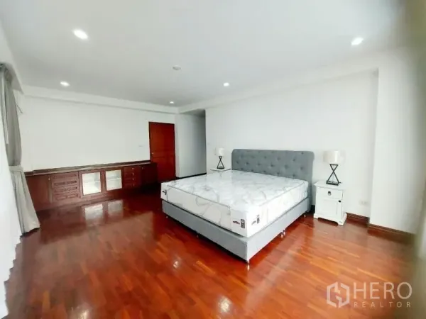 Condominium for rent in Watthana, Bangkok - Spacious bedroom with upholstered bed, bedside tables, built-in cabinets and glossy wood flooring.