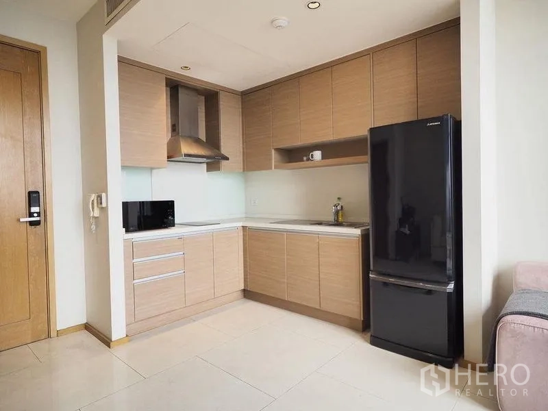 Condominium for rent in Khlong Toei, Bangkok - Compact L-shaped kitchen featuring stainless hood and full-size fridge.