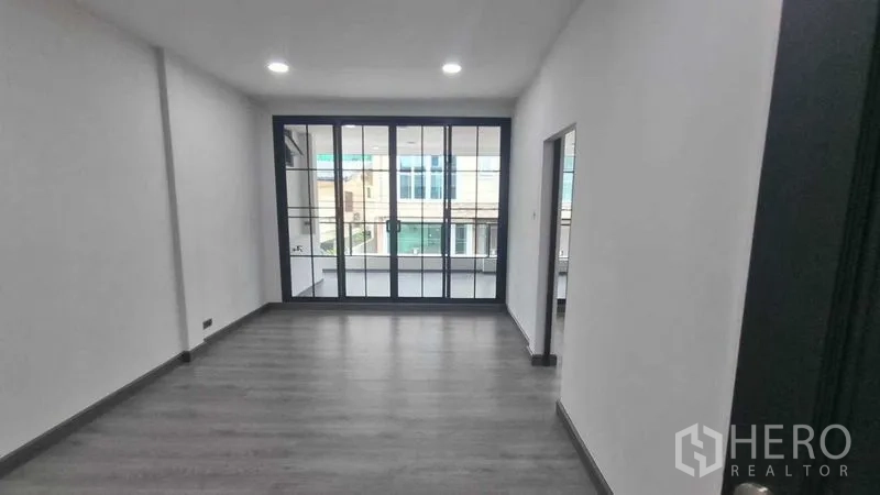 Townhouse for rent in Khlong Toei, Bangkok - Upper floor room opening to the balcony via black-framed sliding doors.