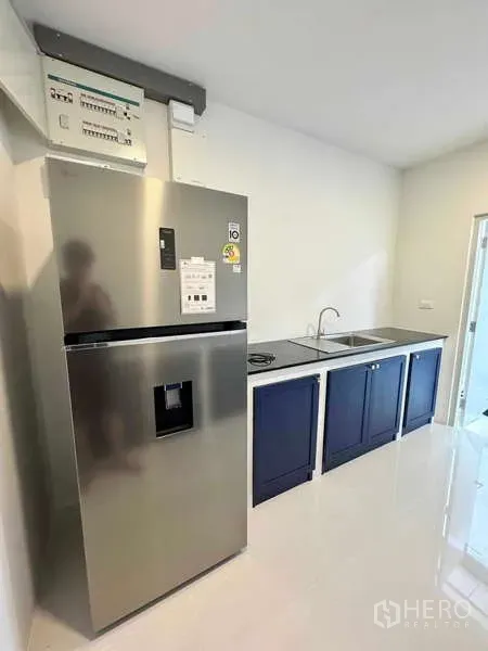 Detached House for rent or sale in Bang Phli, Samut Prakan - Compact kitchen with stainless refrigerator, sink, black countertop and navy lower cabinets.