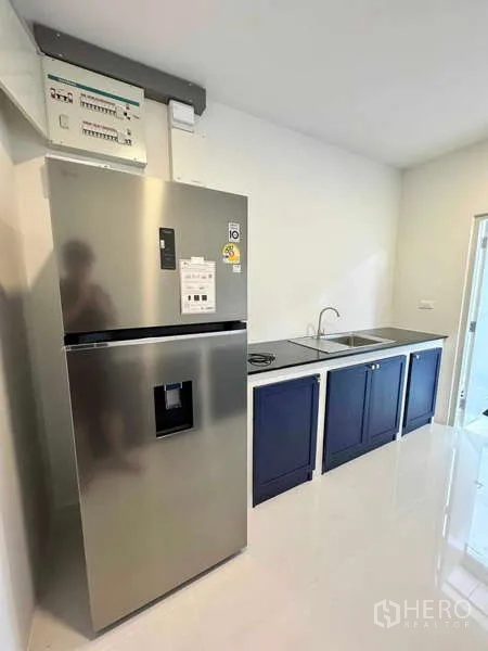 Detached House for rent or sale in Bang Phli, Samut Prakan - Compact kitchen with stainless refrigerator, sink, black countertop and navy lower cabinets.